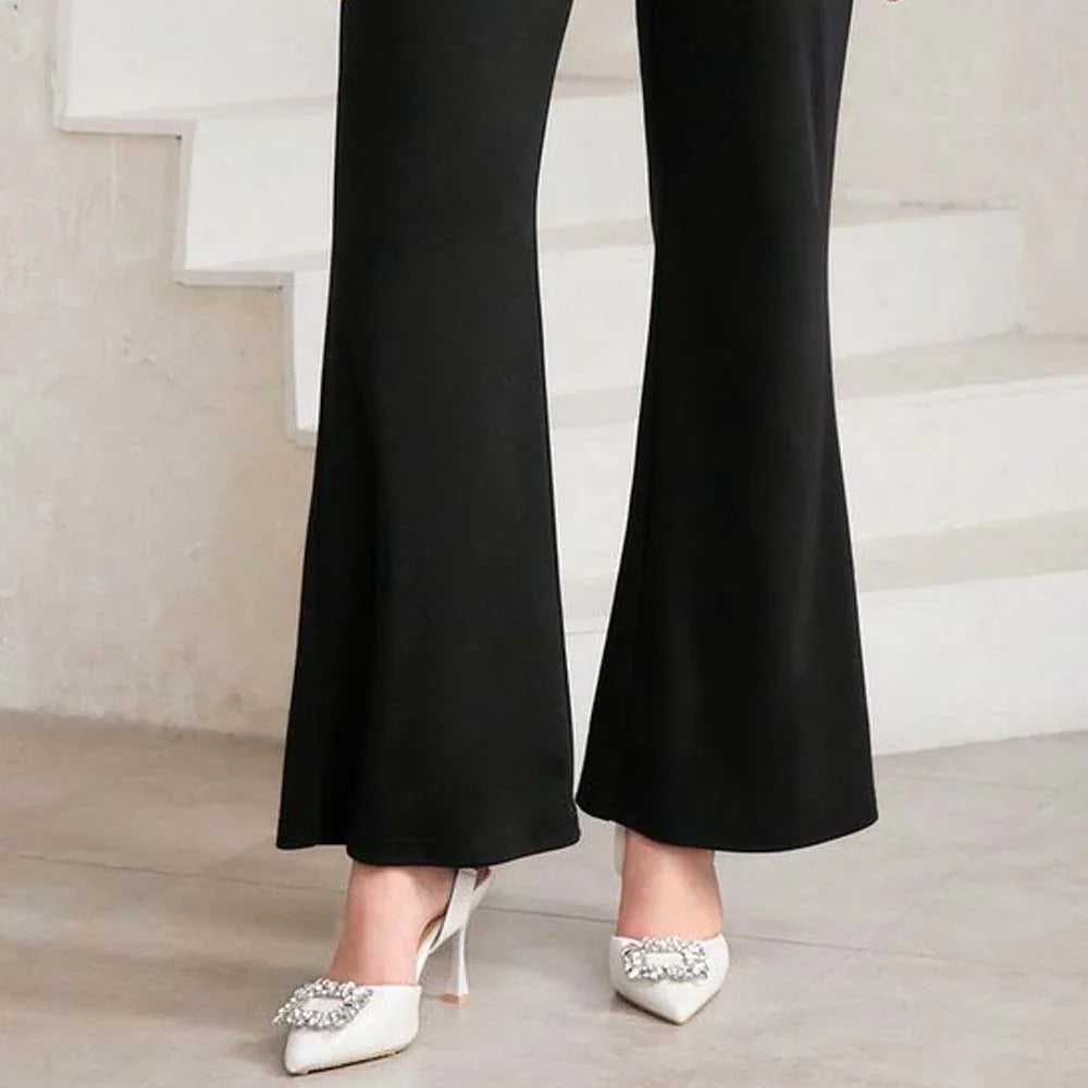 Person wearing black flared trousers stands on a light floor near white stairs. They wear white heels with decorative embellishments, creating a chic, elegant look..