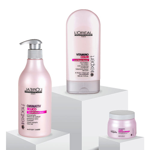 A collection of various hair products on a pink surface with dried grasses. Includes bottles from Dove, TRESemmé, and more, conveying a beauty theme.