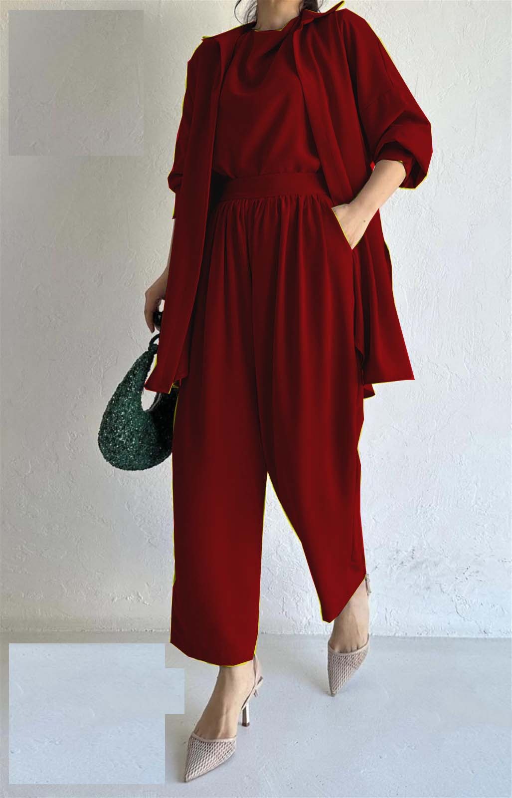 A person is wearing a flowing red ensemble with a matching long coat and pants, holding a textured green handbag. Beige pointed heels add elegance.