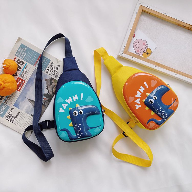 Two cartoon-themed 3D hard shell chest bags for kids with colorful designs, displayed on a white surface with newspaper and framed picture.