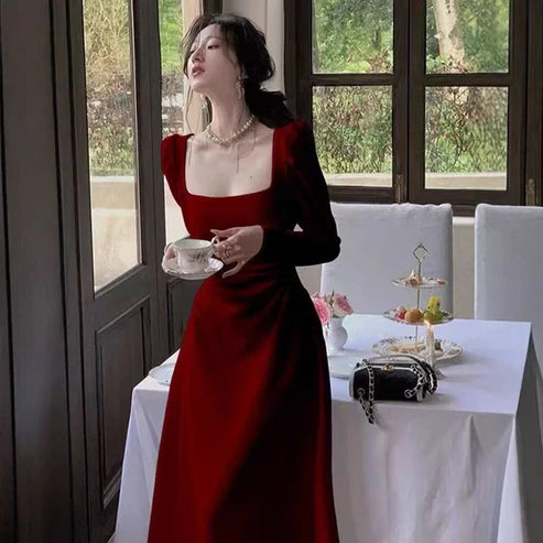 Woman in a red dress holding a teacup in a elegant setting with a table and window.