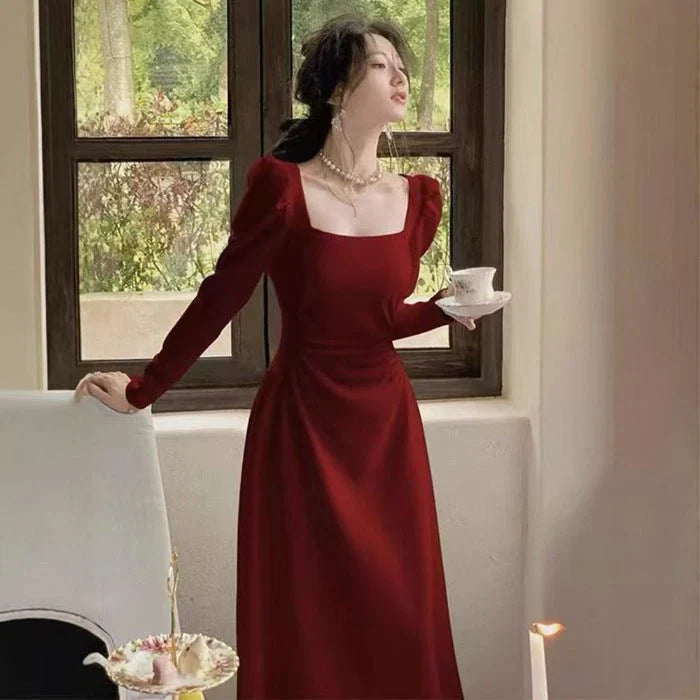 Woman in a red dress holding a teacup in a room with a window and fireplace.
