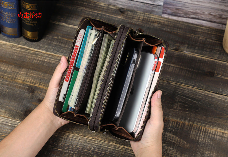 Hand holding an open wallet with money and a phone on a wooden surface