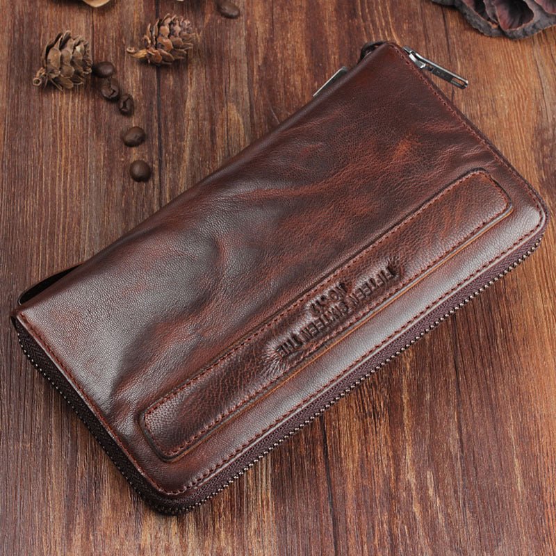 Brown leather wallet on a wooden surface with pine cones.