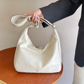 White handbag held by a person wearing a dark suit against a neutral background
