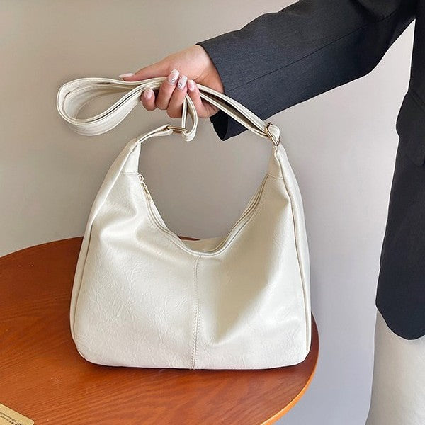White handbag held by a person wearing a dark suit against a neutral background