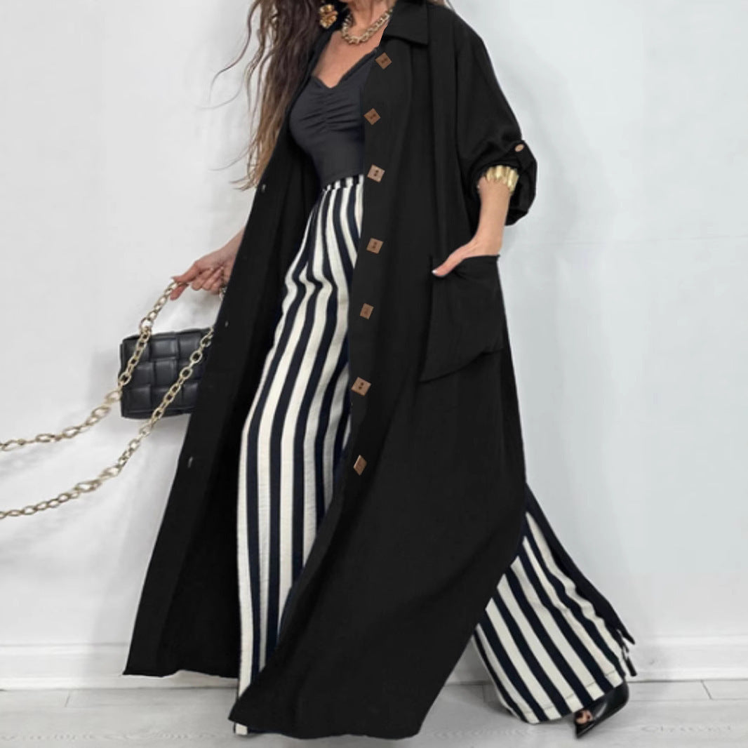 Woman wearing a long black coat over a black and white striped dress, holding a black handbag.