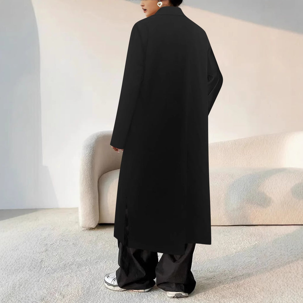 Person wearing a long black coat in a minimalistic room.