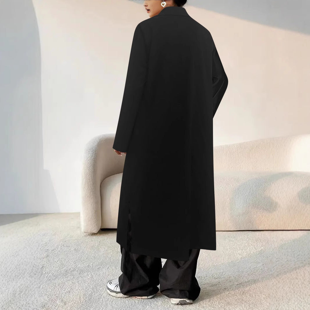 Person wearing a long black coat in a minimalistic room.