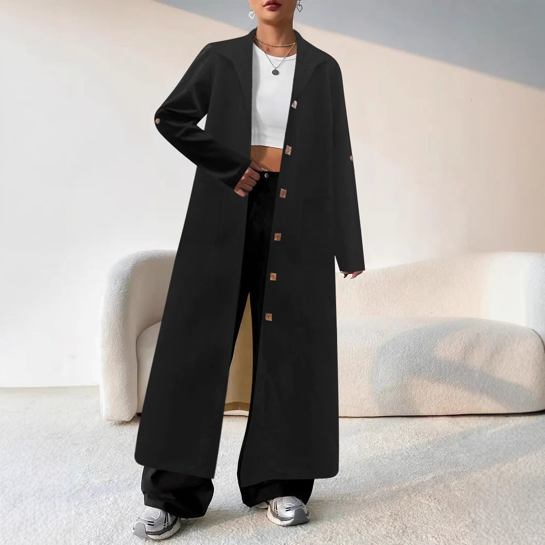 Person wearing a long black coat with brown buttons in a minimalistic room.
