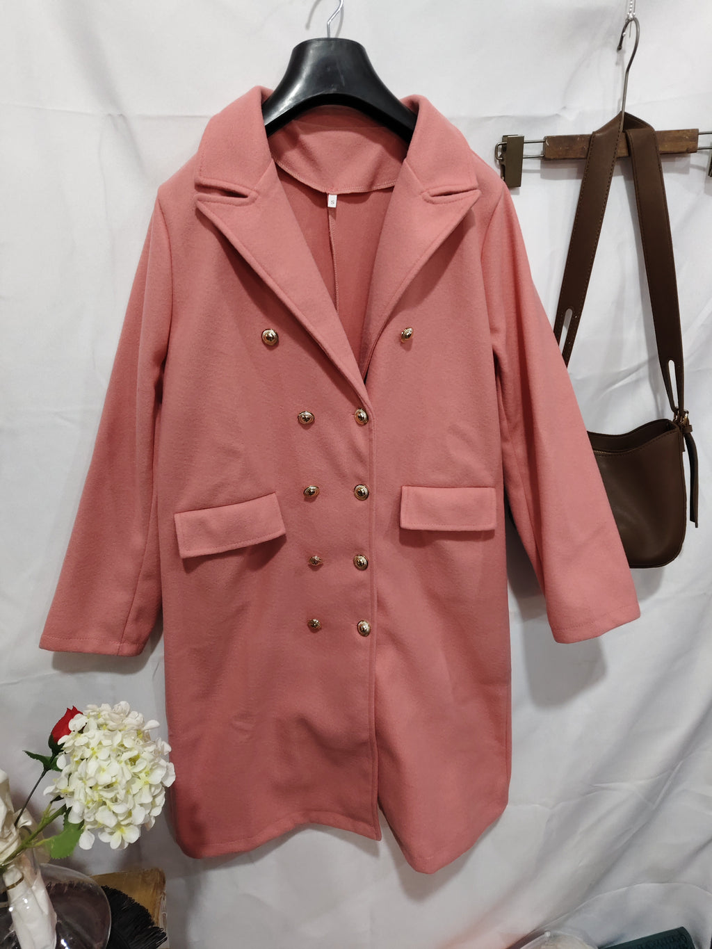 Pink coat with gold buttons on a hanger against a white background