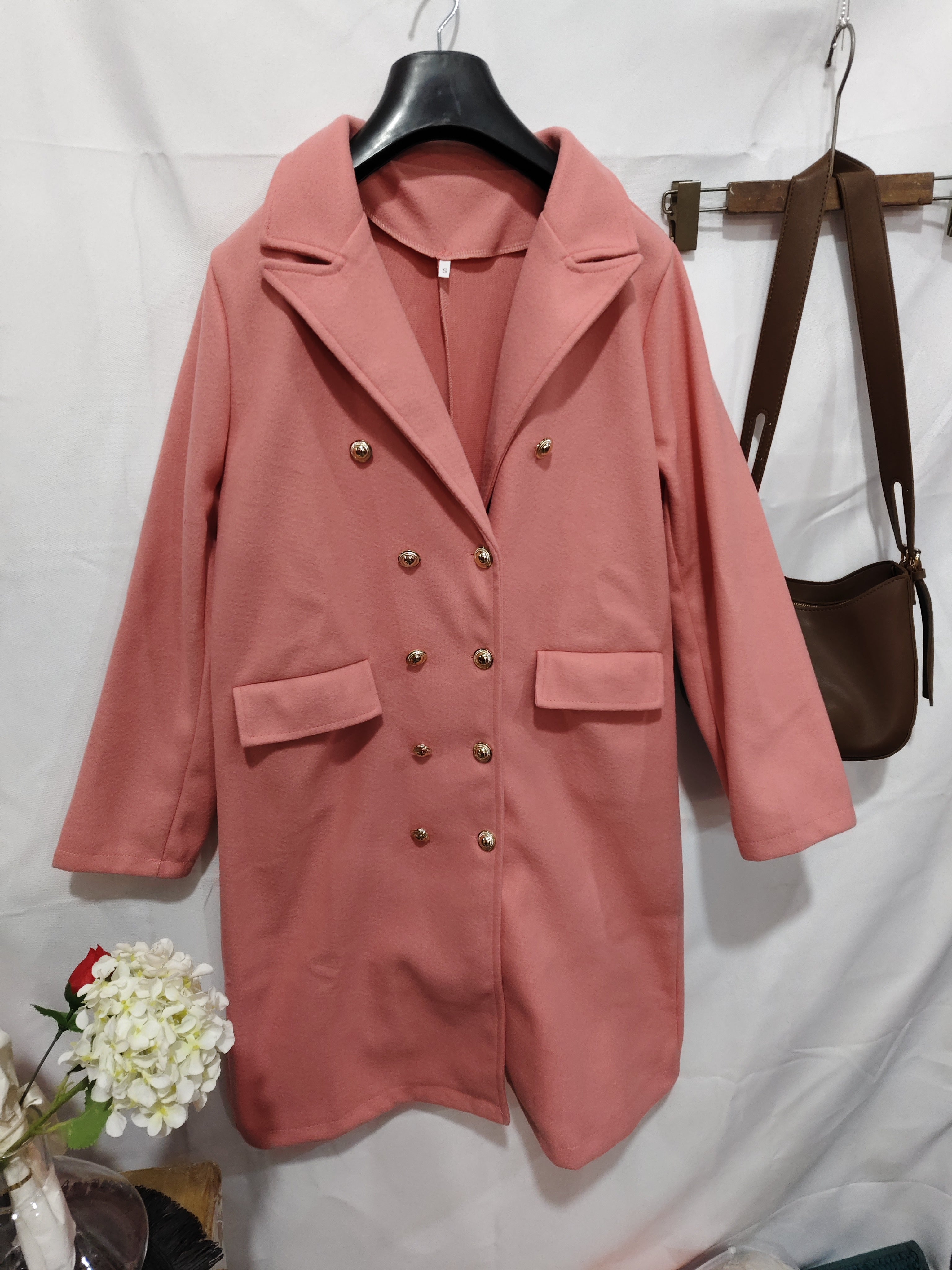 Pink coat with gold buttons on a hanger against a white background